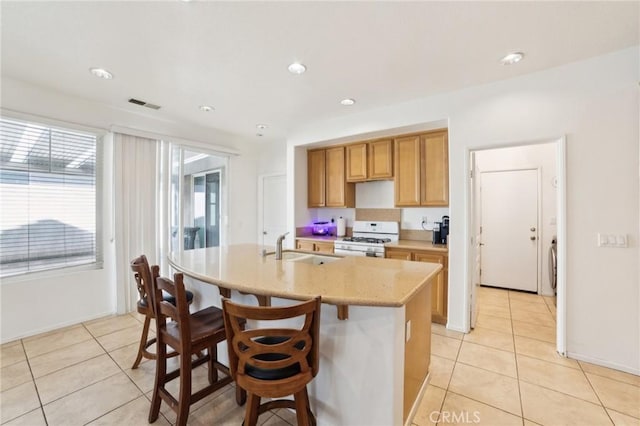 kitchen with light tile patterned floors, white gas stove, a kitchen island with sink, a sink, and visible vents