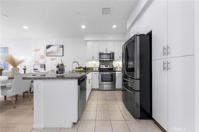 kitchen featuring stainless steel appliances, light tile patterned flooring, dark stone countertops, white cabinets, and sink