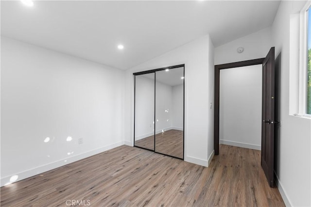 unfurnished bedroom with a closet, lofted ceiling, and light hardwood / wood-style flooring