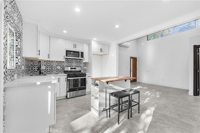 kitchen with white cabinetry, a wall unit AC, decorative backsplash, gas stove, and a kitchen breakfast bar