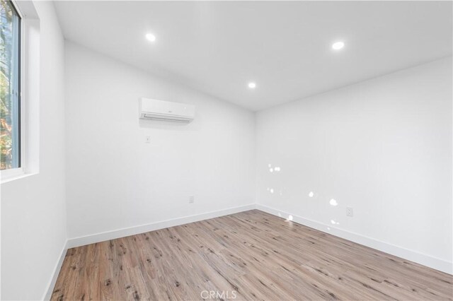 spare room with vaulted ceiling, a wall unit AC, and light wood-type flooring