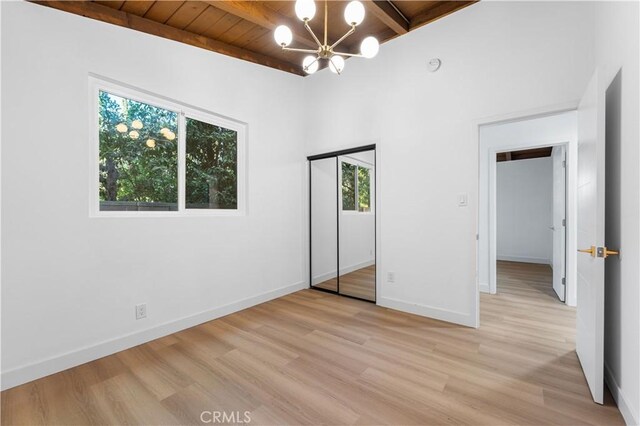 unfurnished bedroom featuring wood ceiling, a closet, a chandelier, light hardwood / wood-style flooring, and beam ceiling