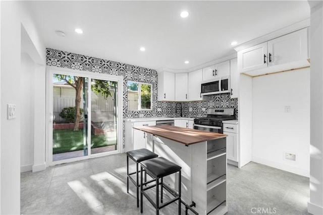 kitchen featuring backsplash, wooden counters, white cabinetry, a kitchen breakfast bar, and stainless steel appliances