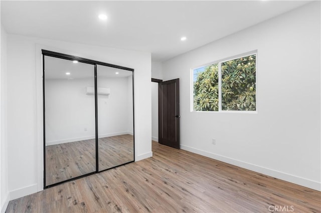 unfurnished bedroom with a closet, a wall mounted air conditioner, vaulted ceiling, and light hardwood / wood-style flooring