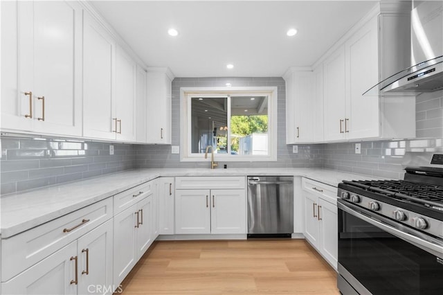 kitchen featuring wall chimney exhaust hood, light stone counters, stainless steel appliances, and white cabinetry