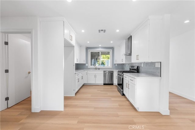 kitchen featuring wall chimney range hood, decorative backsplash, sink, stainless steel appliances, and white cabinets