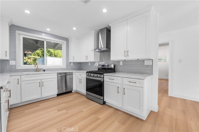 kitchen with wall chimney exhaust hood, sink, stainless steel appliances, and white cabinetry