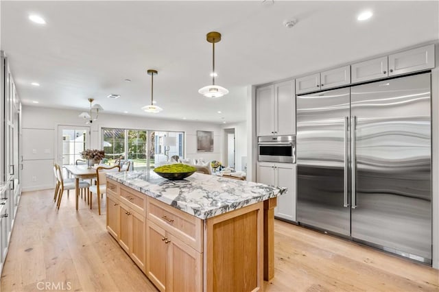 kitchen with hanging light fixtures, stainless steel appliances, light hardwood / wood-style floors, light stone countertops, and a kitchen island