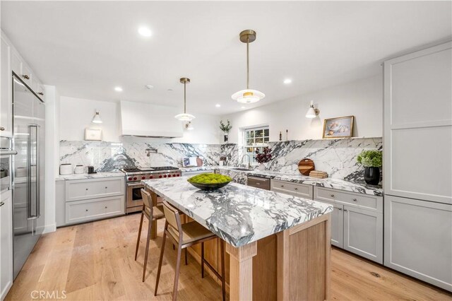 kitchen featuring pendant lighting, custom range hood, white cabinetry, a kitchen island, and high end appliances