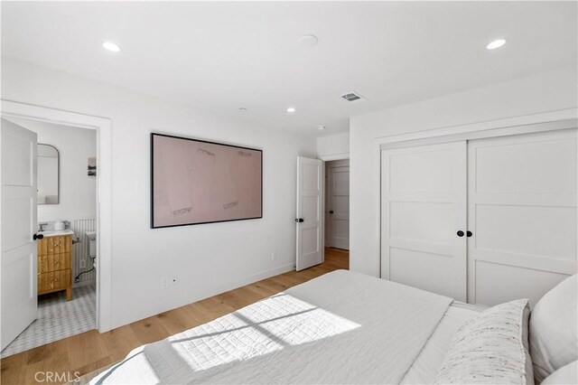 bedroom featuring radiator, ensuite bathroom, a closet, and light wood-type flooring