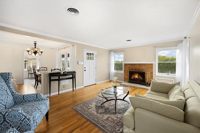 living room with visible vents, baseboards, light wood-style floors, a brick fireplace, and crown molding