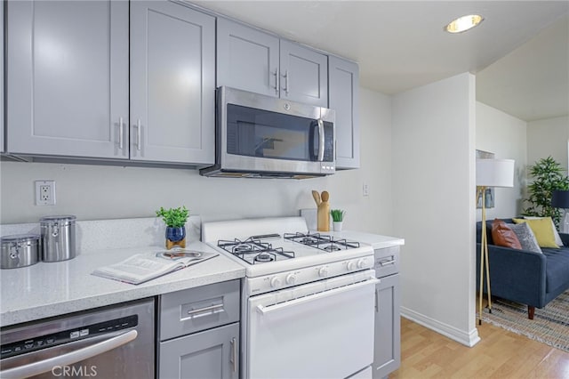 kitchen with appliances with stainless steel finishes, gray cabinetry, and light hardwood / wood-style flooring