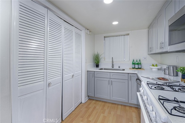 kitchen with light wood-type flooring, gray cabinetry, white range with gas stovetop, and sink