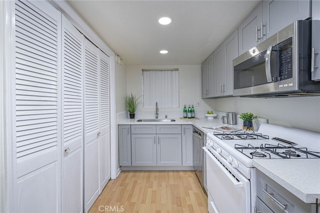 kitchen with light wood-type flooring, gray cabinets, stainless steel appliances, and sink