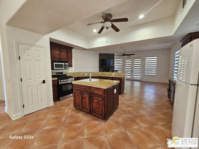 kitchen featuring white fridge, light tile patterned floors, a kitchen island with sink, dark brown cabinets, and stainless steel range oven