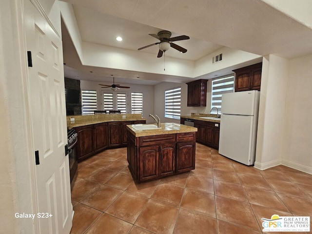 kitchen featuring white refrigerator, a center island with sink, dark brown cabinetry, and sink