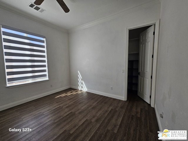 unfurnished bedroom featuring ceiling fan, dark hardwood / wood-style floors, a spacious closet, and crown molding