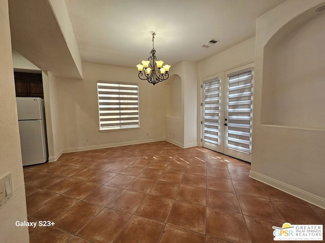 unfurnished dining area with french doors, dark tile patterned flooring, and a notable chandelier