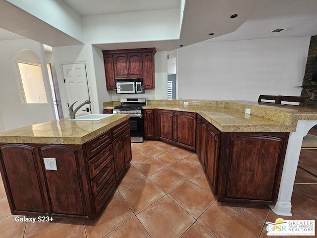 kitchen featuring light tile patterned floors, stainless steel stove, dark brown cabinets, and sink