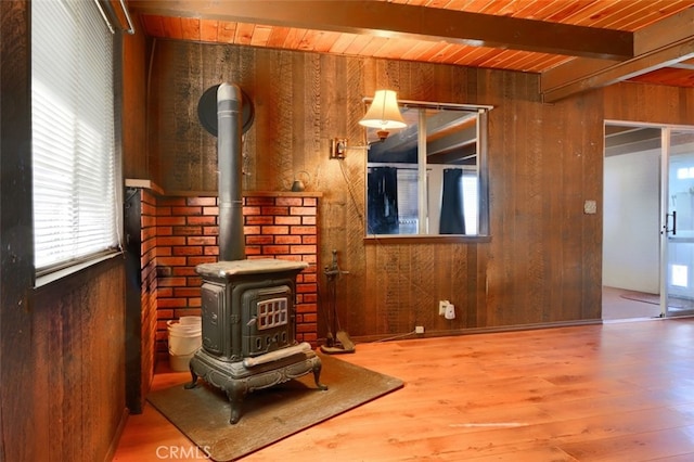 living room featuring wooden ceiling, beam ceiling, a wood stove, and wood walls