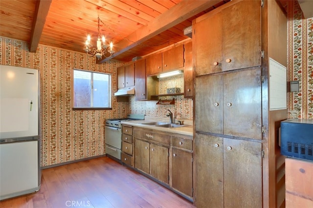 kitchen featuring high end stainless steel range oven, a notable chandelier, white refrigerator, pendant lighting, and beamed ceiling