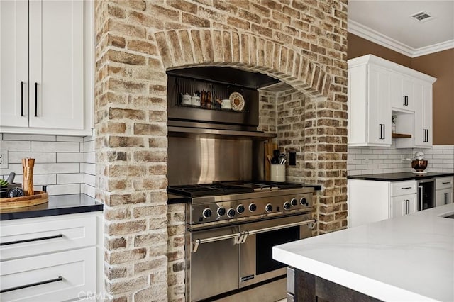 kitchen with white cabinetry, crown molding, backsplash, and high end range