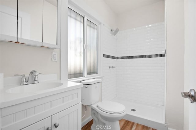 bathroom featuring toilet, hardwood / wood-style floors, tiled shower, and vanity