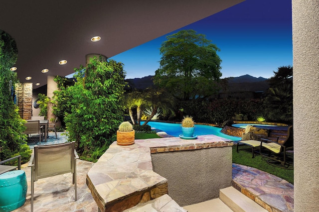 patio terrace at dusk featuring a swimming pool with hot tub and a mountain view