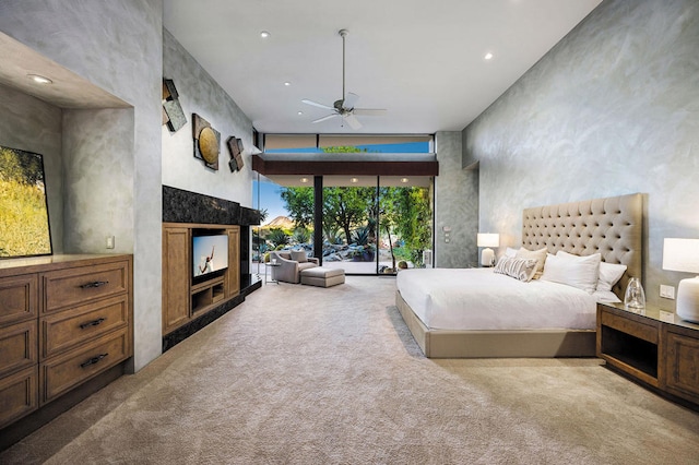 bedroom with floor to ceiling windows, ceiling fan, access to outside, a towering ceiling, and light colored carpet