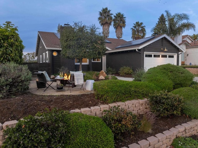 single story home with a garage, a patio area, a fire pit, and solar panels