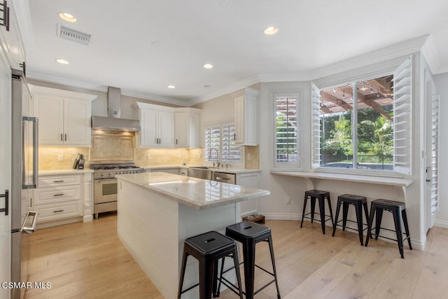 kitchen with a kitchen breakfast bar, white cabinetry, premium appliances, and wall chimney range hood