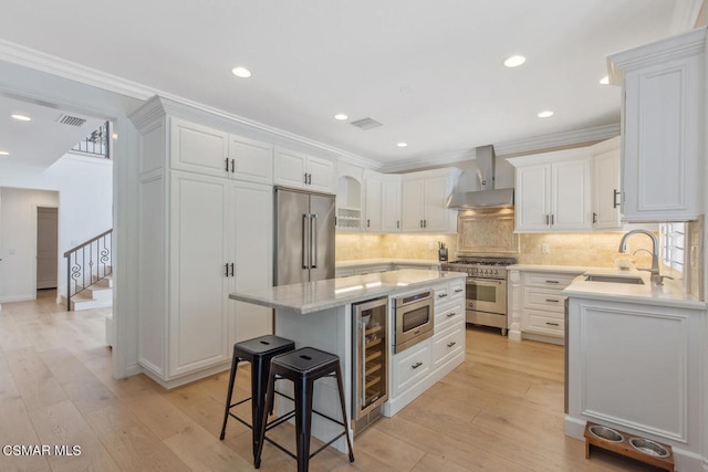 kitchen featuring premium appliances, white cabinets, a center island, wall chimney range hood, and sink