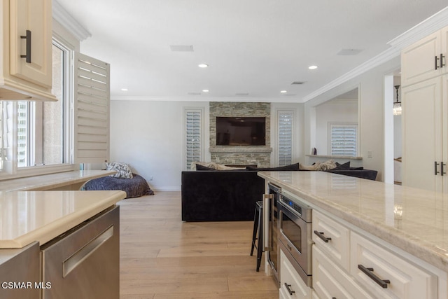 kitchen with a fireplace, light hardwood / wood-style floors, a kitchen bar, ornamental molding, and light stone counters