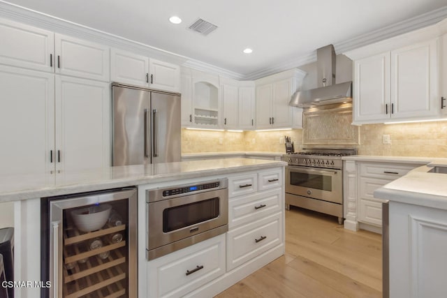 kitchen featuring white cabinets, beverage cooler, wall chimney exhaust hood, high end appliances, and decorative backsplash