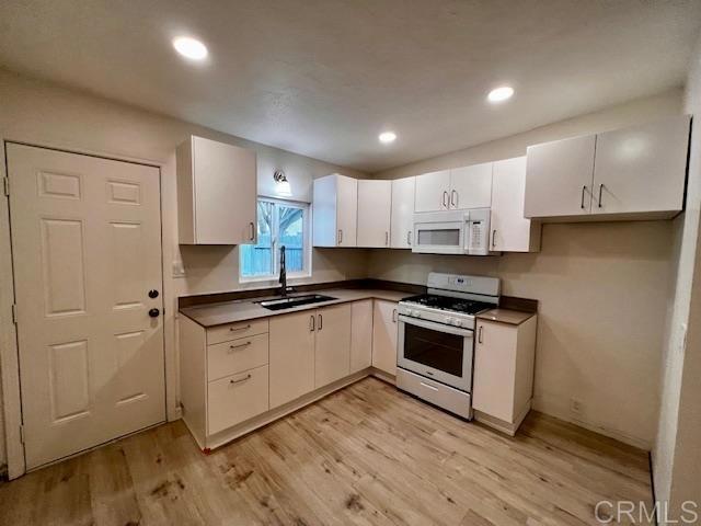 kitchen featuring light wood-type flooring, white cabinetry, sink, and white appliances