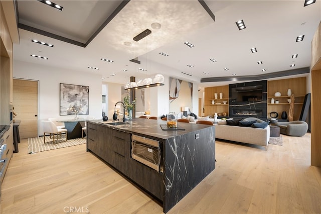 kitchen with a large island, sink, a fireplace, light hardwood / wood-style floors, and a raised ceiling