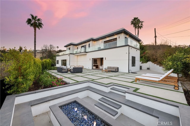 back house at dusk featuring a patio area and an outdoor living space with a fire pit