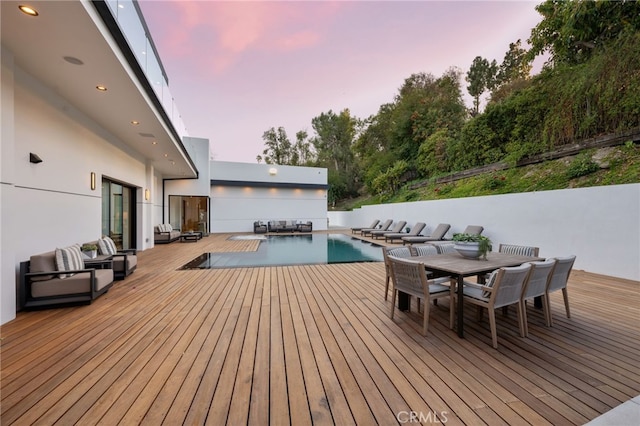 deck at dusk with an outdoor hangout area and a fenced in pool