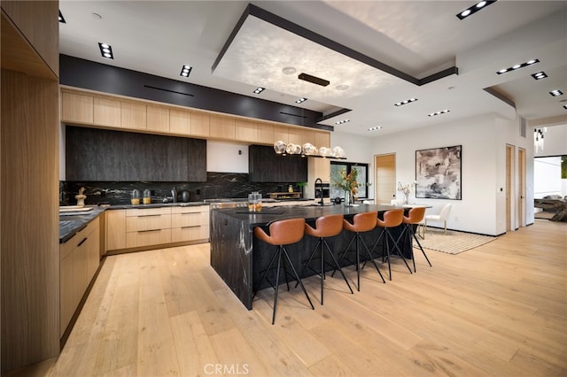 kitchen featuring a kitchen island with sink, a breakfast bar area, light brown cabinetry, and light wood-type flooring