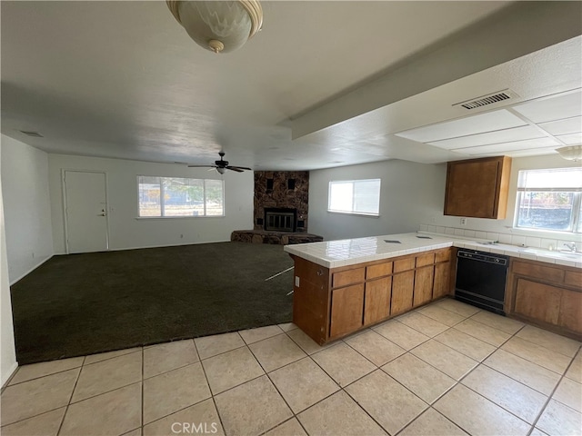 kitchen with dishwasher, a fireplace, kitchen peninsula, ceiling fan, and light colored carpet