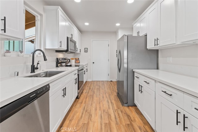 kitchen with stainless steel appliances, white cabinetry, sink, and light wood-type flooring