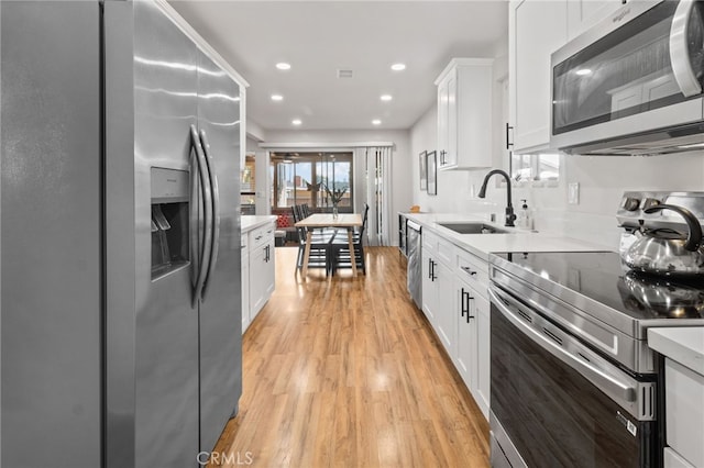 kitchen featuring white cabinetry, sink, light wood-type flooring, and appliances with stainless steel finishes