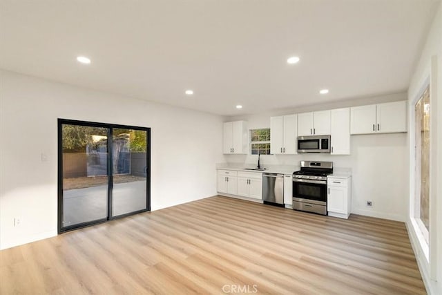 kitchen with appliances with stainless steel finishes, light hardwood / wood-style flooring, white cabinets, and sink