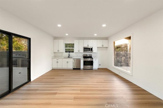 kitchen with white cabinets, appliances with stainless steel finishes, sink, and light wood-type flooring