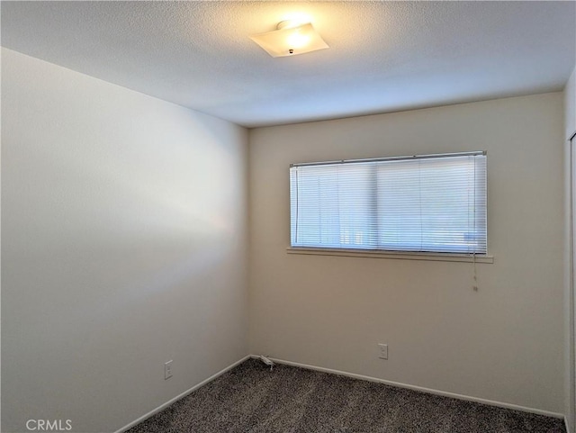 empty room with a textured ceiling, baseboards, and dark colored carpet