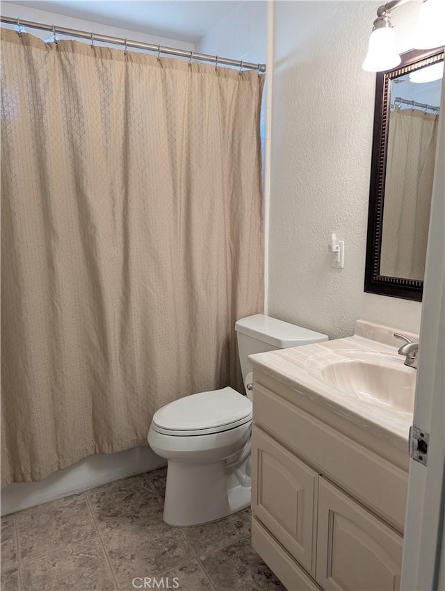 bathroom with vanity, toilet, a textured wall, and tile patterned flooring