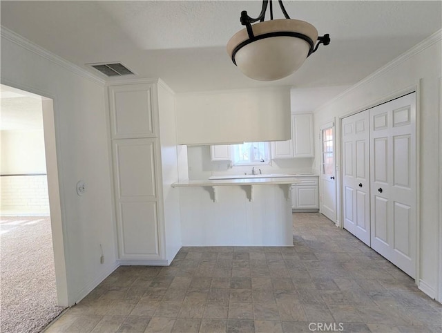 kitchen featuring visible vents, light colored carpet, a breakfast bar area, light countertops, and white cabinets