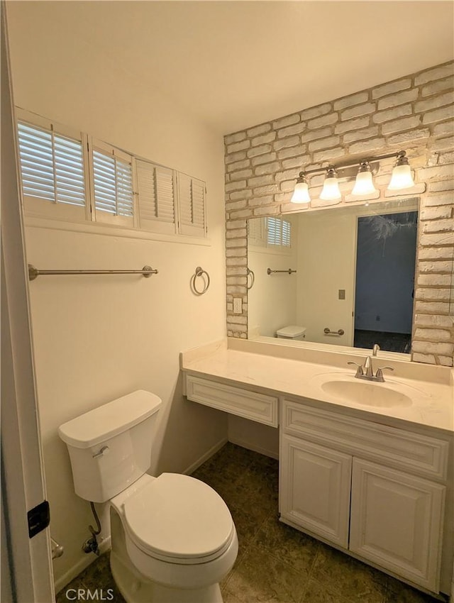 bathroom with baseboards, toilet, brick wall, and vanity