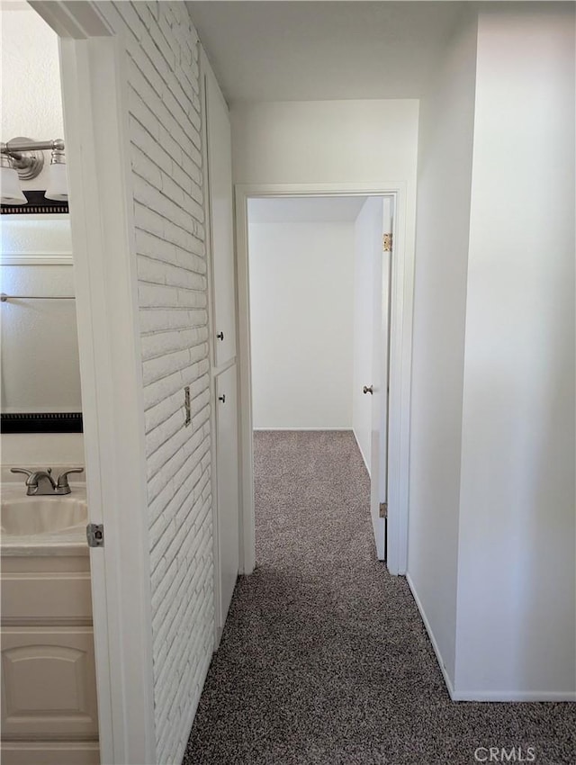 hall featuring carpet flooring, baseboards, and a sink