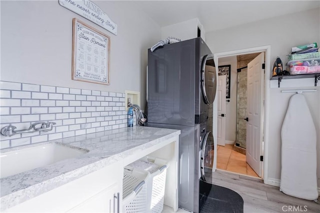 clothes washing area featuring light hardwood / wood-style floors, stacked washer and clothes dryer, and sink